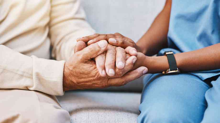 Carer holds hands with an elderly patient.